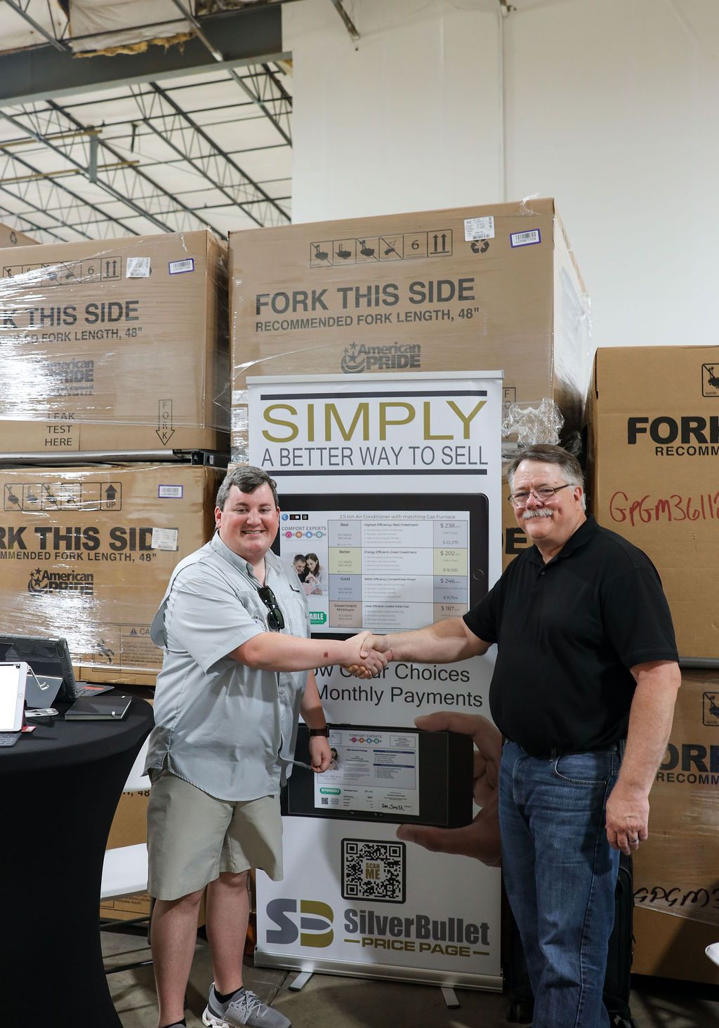 Two men are shaking hands in front of a sign that says `` simply the way to sell ''.