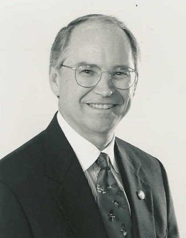 A man in a suit and tie is smiling in a black and white photo.