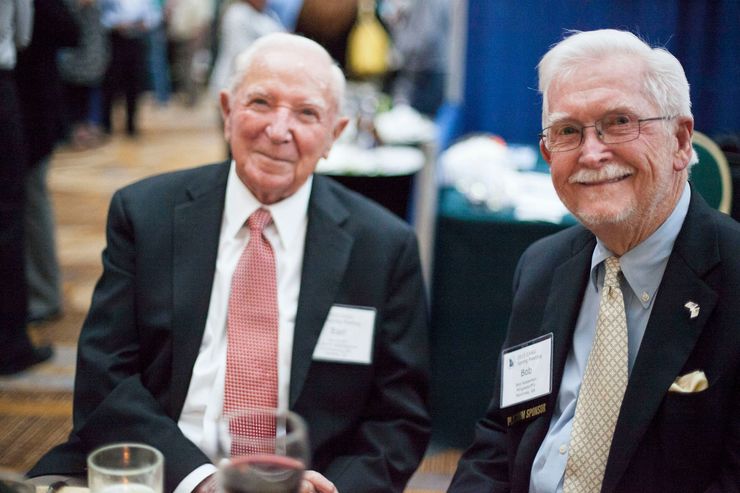 Two men in suits and ties are sitting at a table with wine glasses.