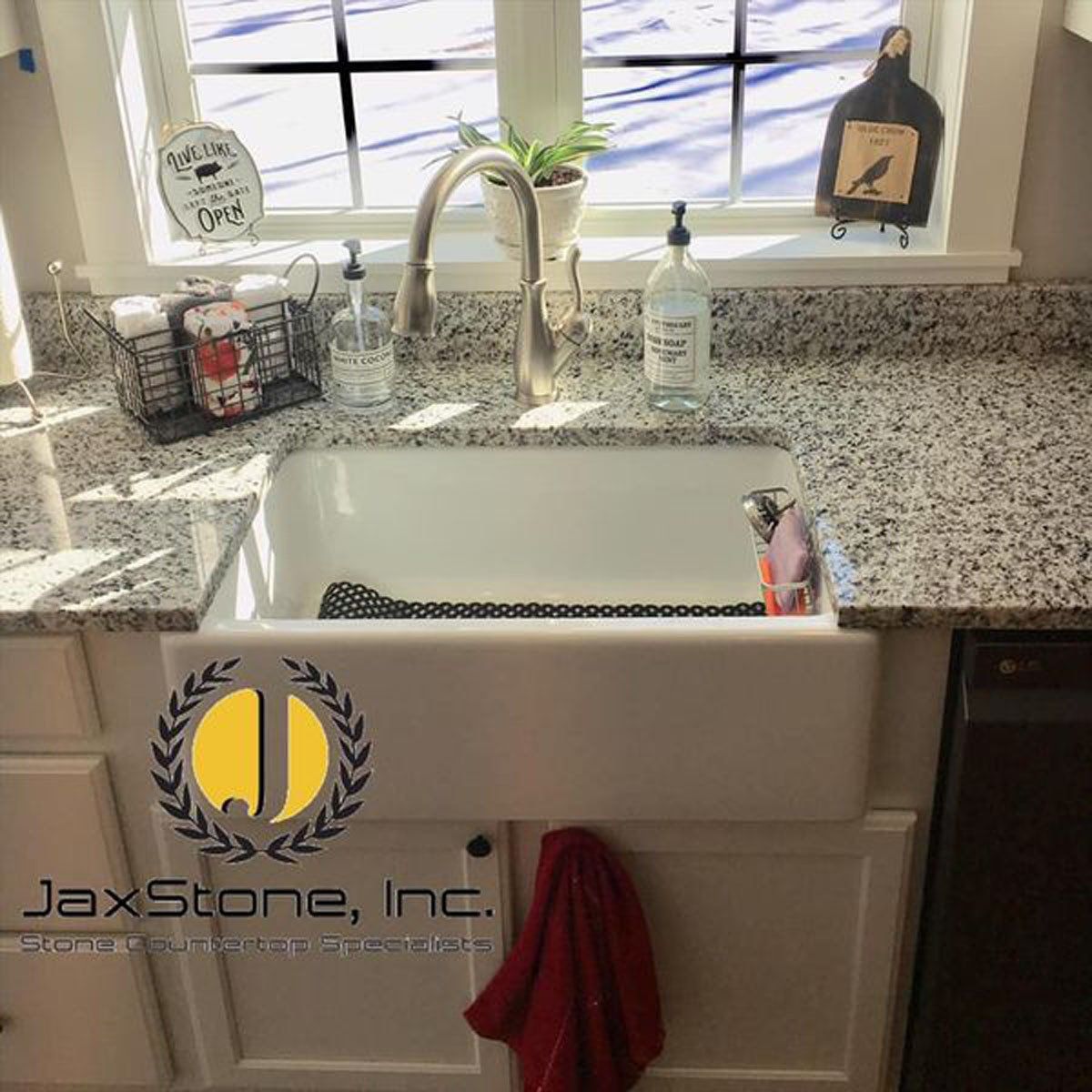 A kitchen with a sink and a window with a logo for jaxstone inc.