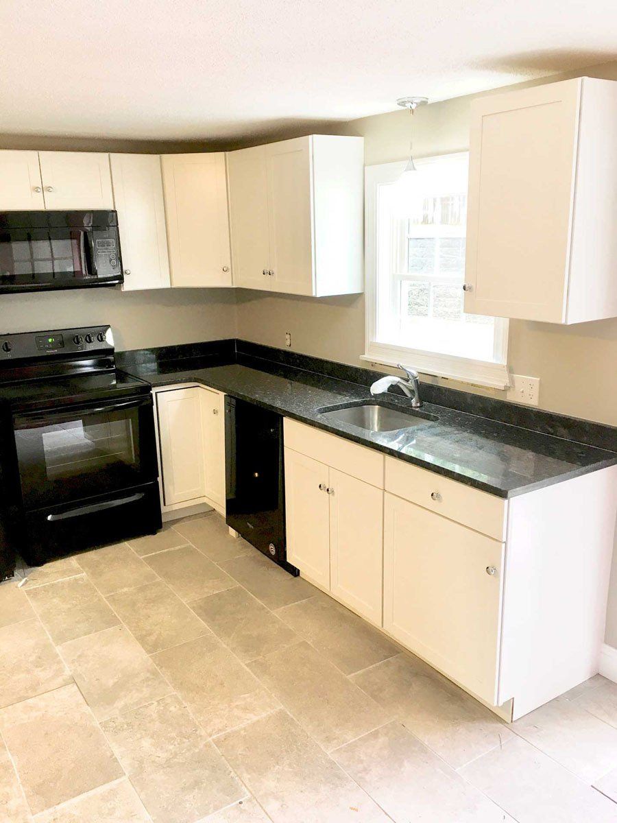 A kitchen with white cabinets , black appliances , a sink , and a window.