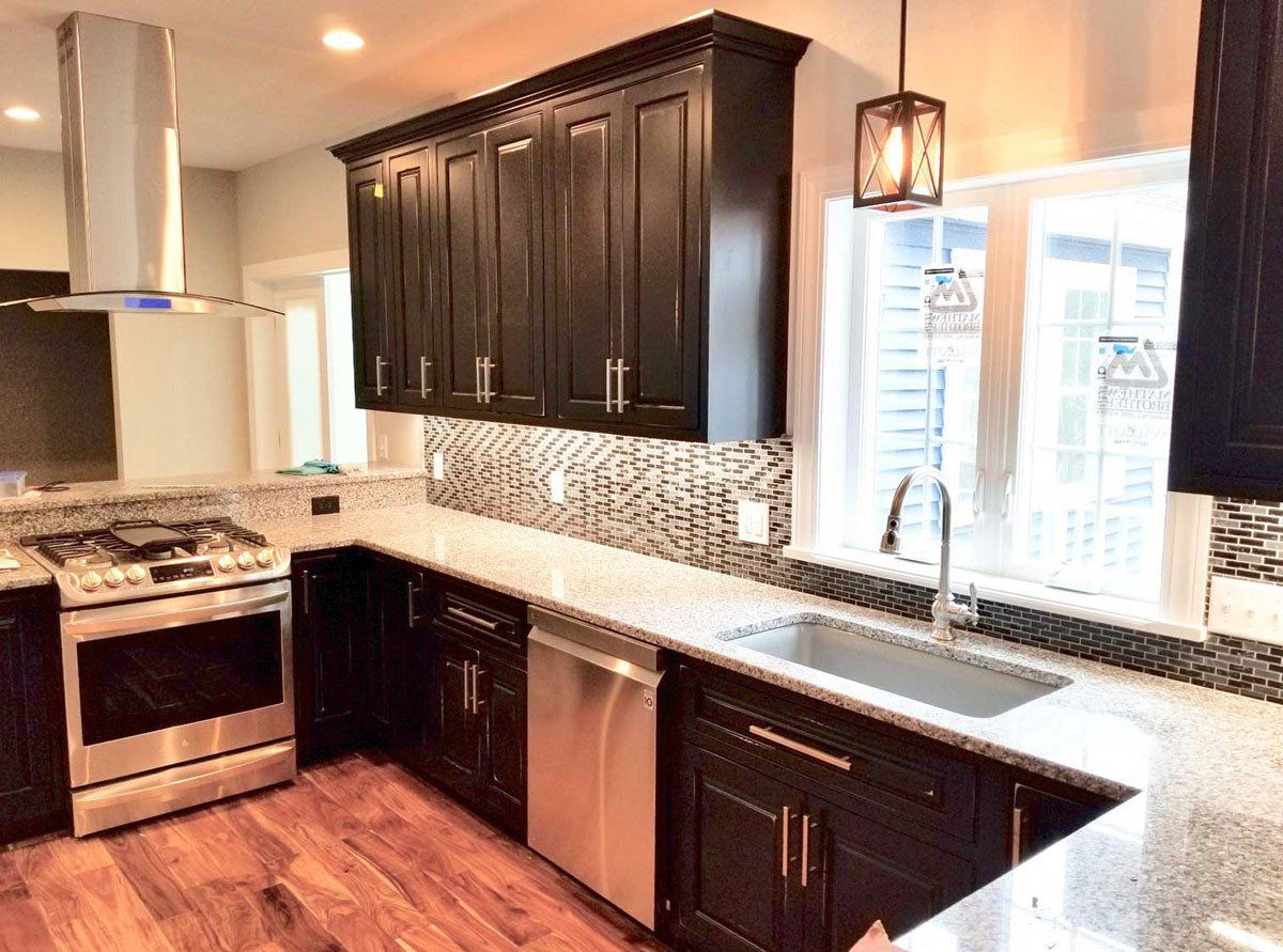 A kitchen with black cabinets , stainless steel appliances , a sink , and a stove.