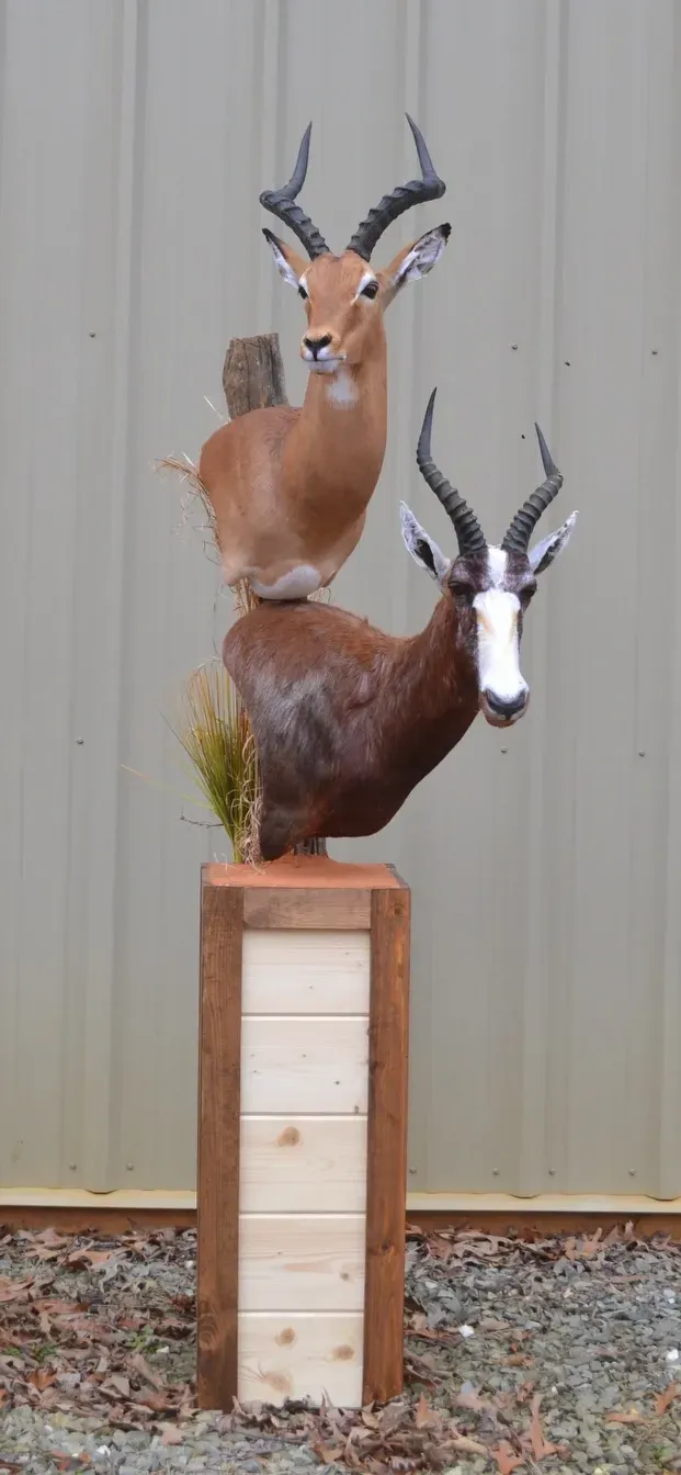 A statue of three deer standing on top of each other on a wooden pedestal.