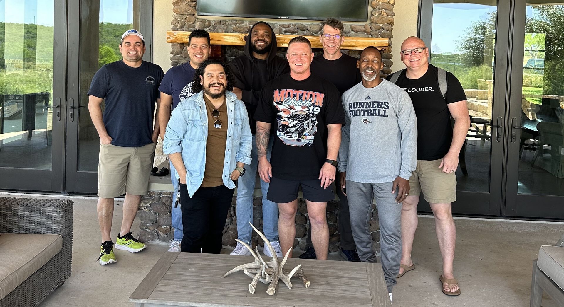 A group of eight people standing together on a covered patio in front of a stone fireplace, smiling for a group photo.