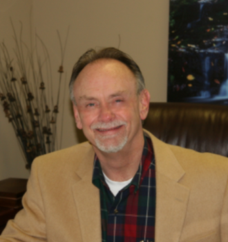 A man in a tan jacket and plaid shirt smiles for the camera