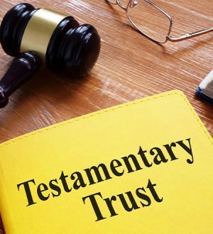 A yellow testamentary trust book is on a wooden table next to a gavel and glasses.