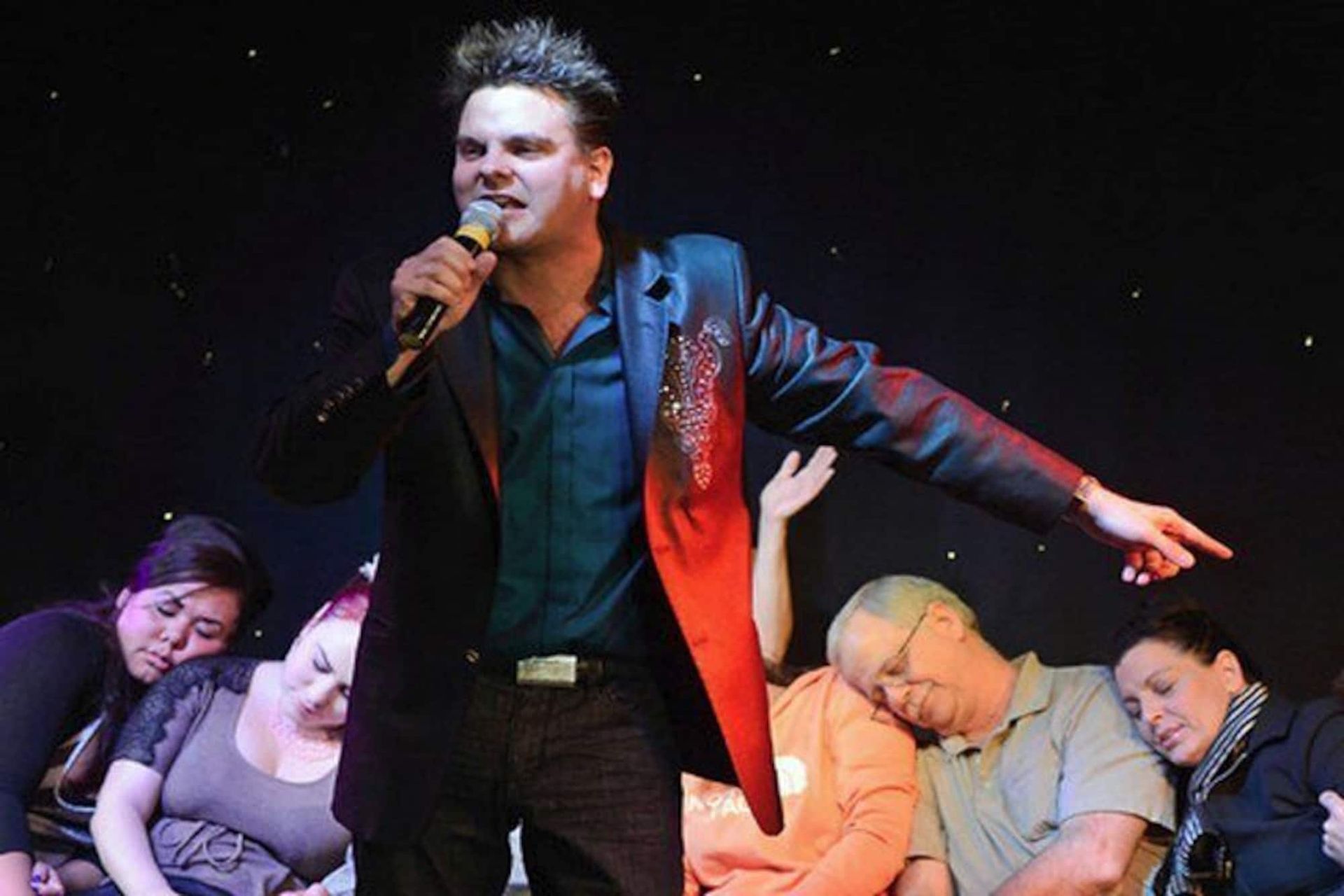 a man in a suit is singing into a microphone while a group of people watch .