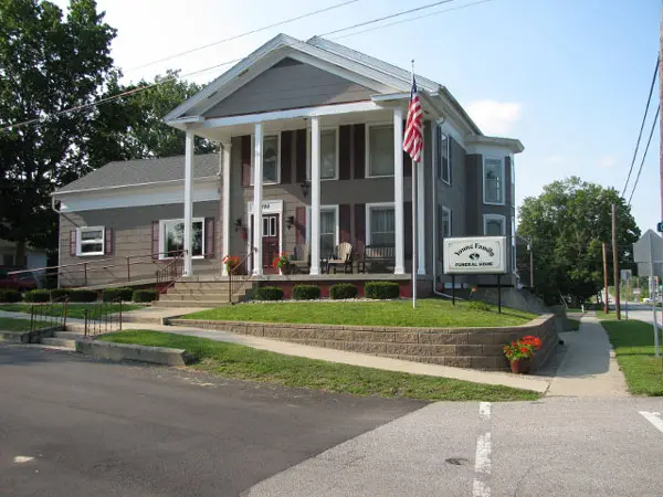 Gray building with white columns and sign. American flag. Raised brick planter.