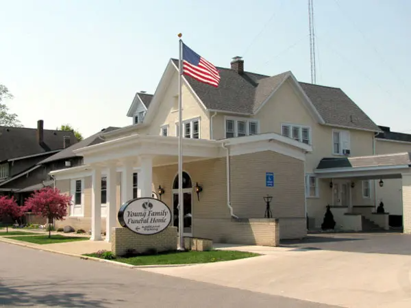 Funeral home with an American flag. Beige building with columns and a sign.