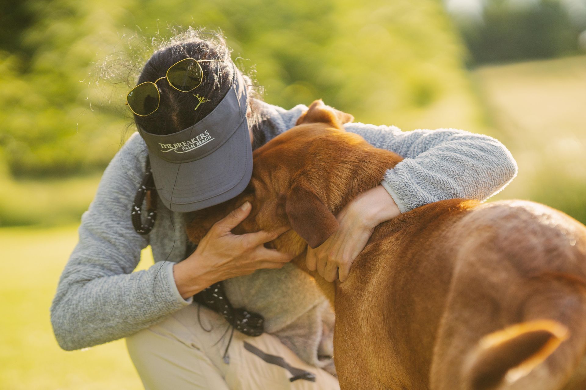 A woman wearing a hat is petting a brown dog.