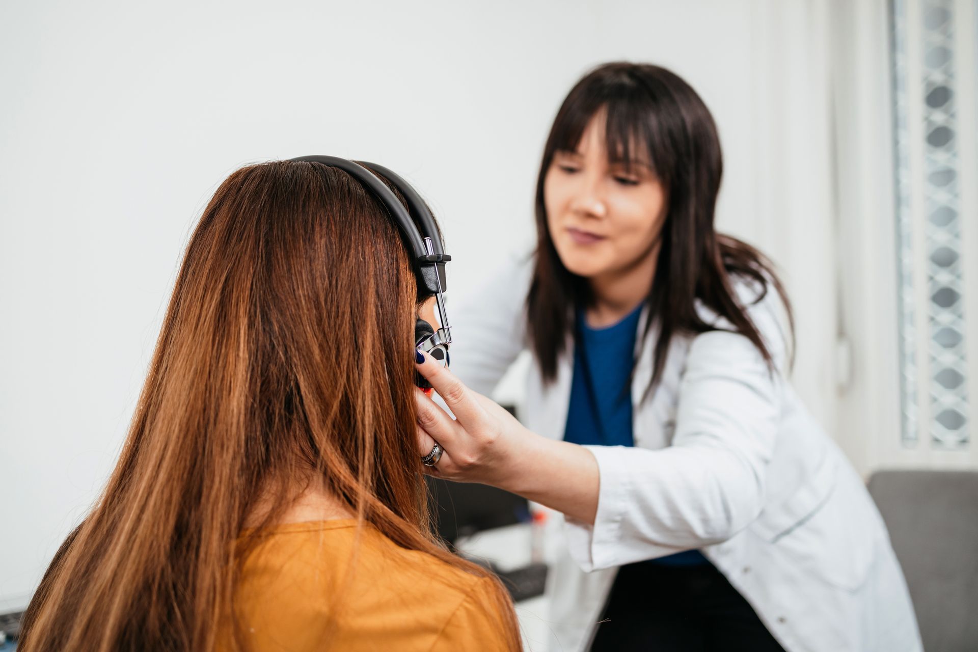 A doctor adjusts headphones on a patient's head, likely for a hearing test, in a light-filled room.