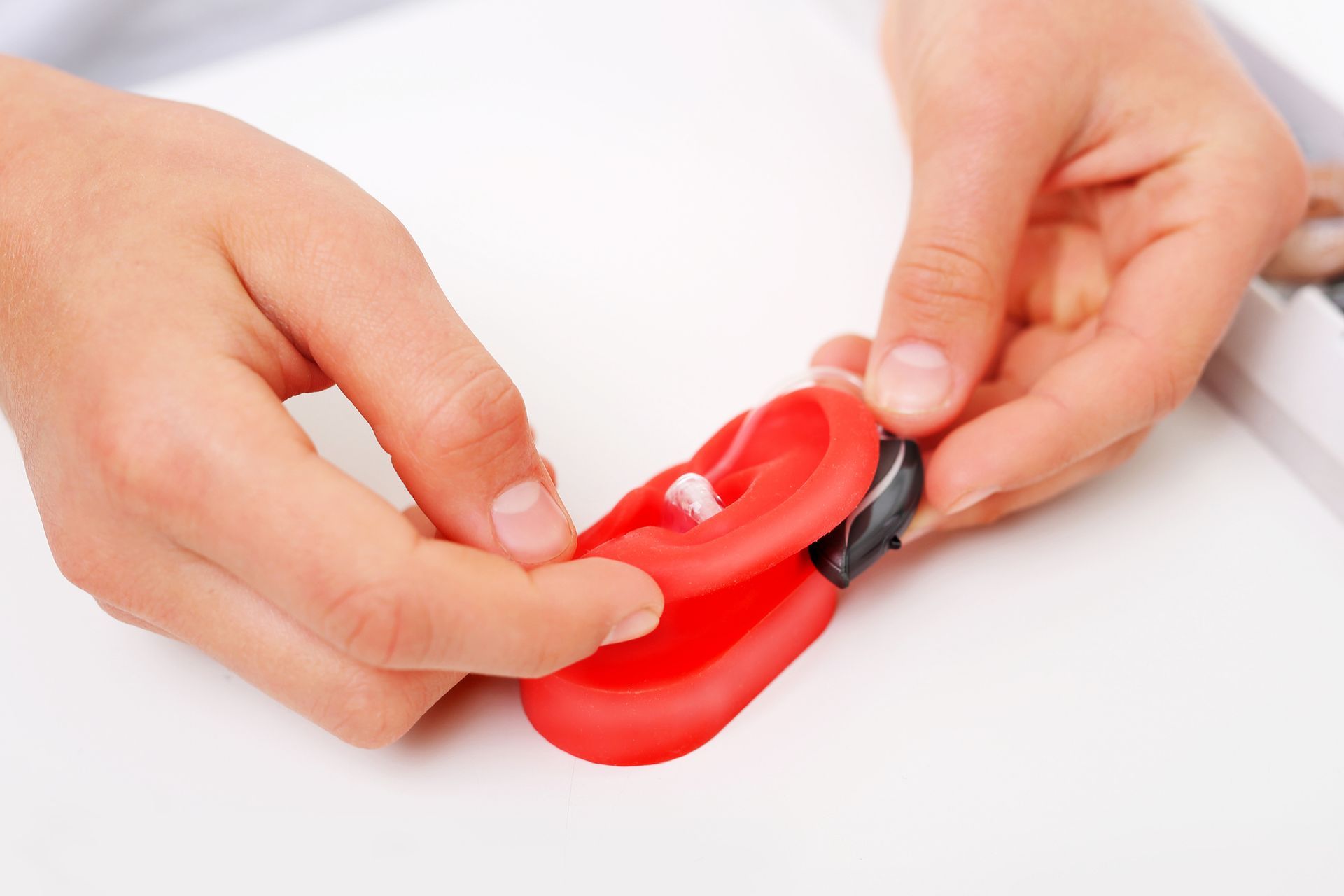 Person in white lab coat holding two beige hearing aids in their palms.