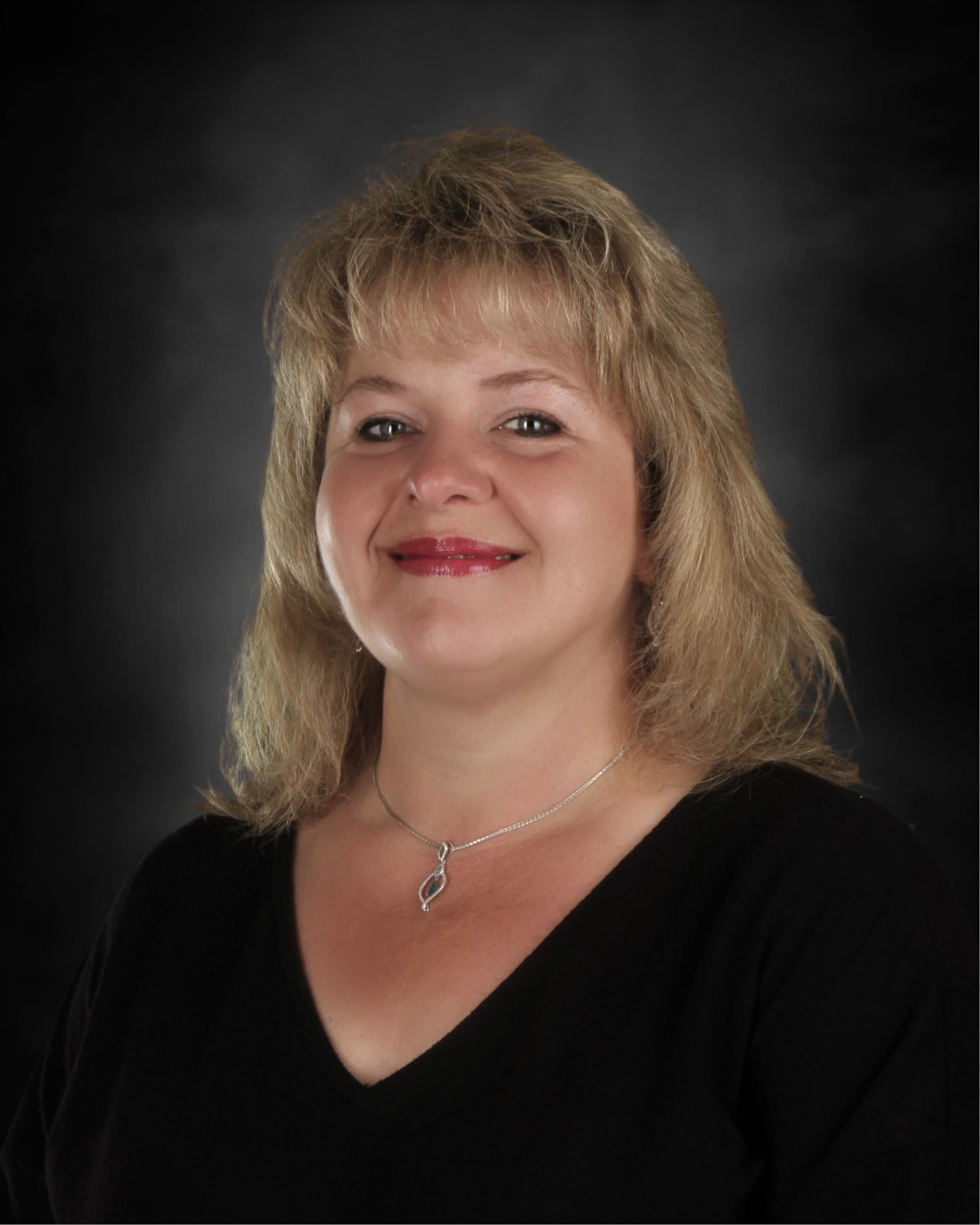 Woman with shoulder-length blonde hair smiling, wearing a black blazer, against a brown mottled background.