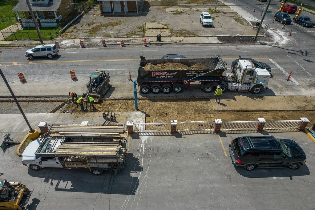 Aerial view of road construction with trucks, workers, and traffic on a divided street