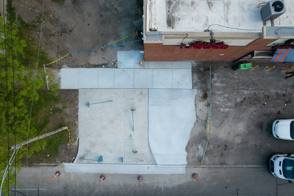 Aerial view of a large concrete courtyard beside a building, with trees and parked cars along the edge.