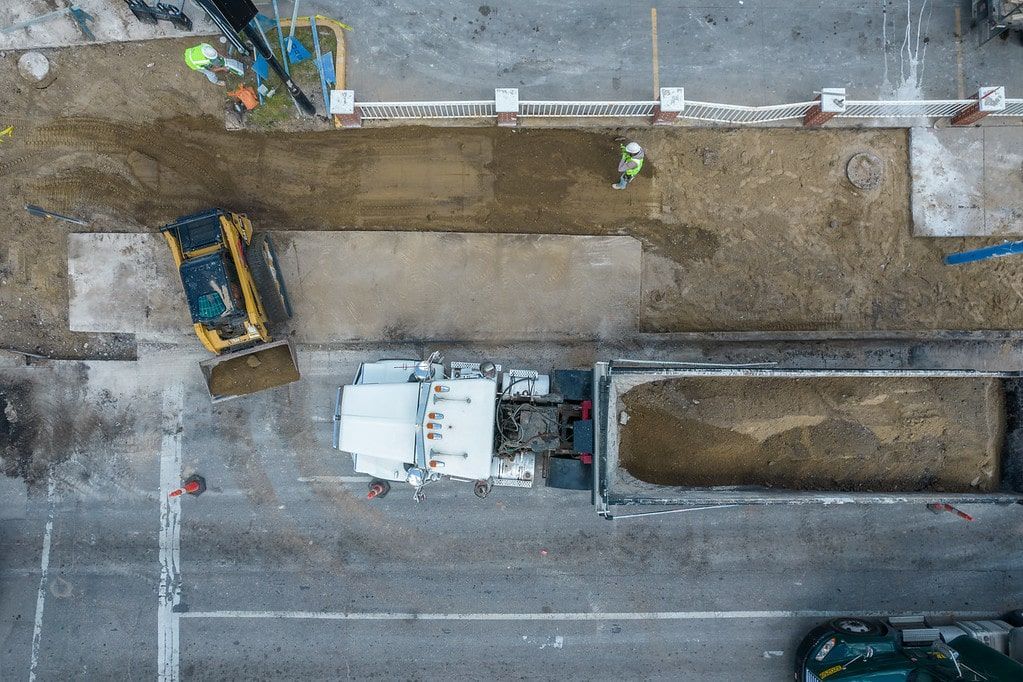 Aerial view of a construction site with excavators, dirt trenches, and a road along the bottom edge