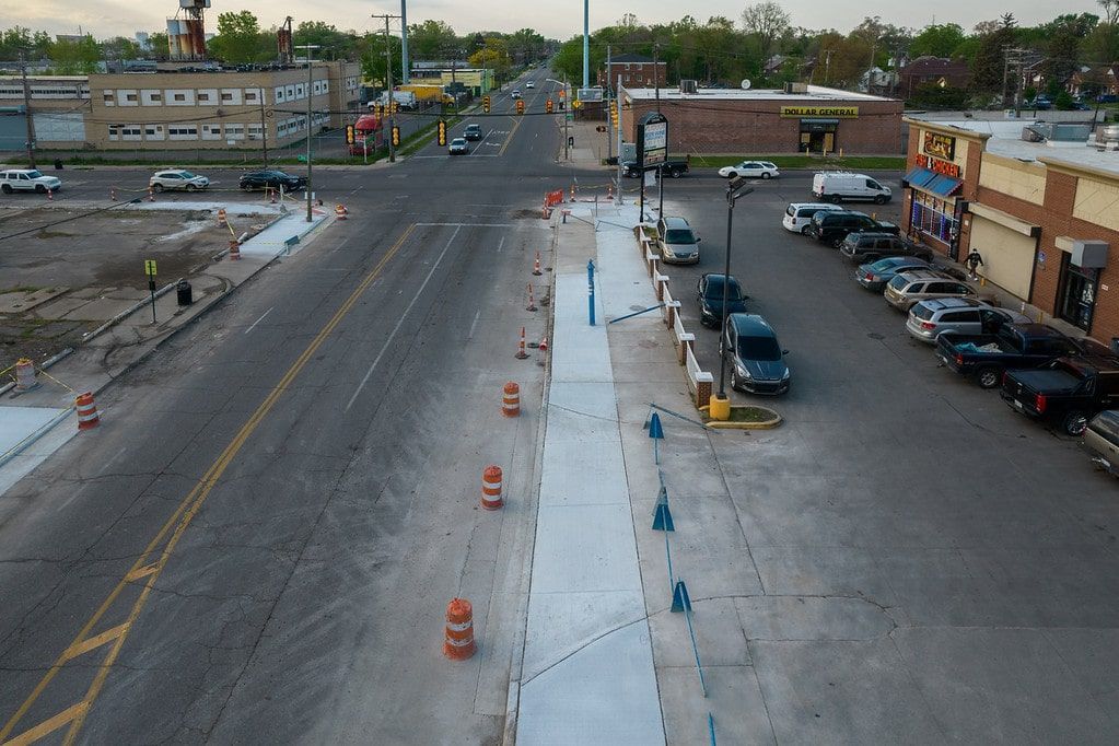 Road construction site with orange cones, concrete barriers, and parked cars beside a street.