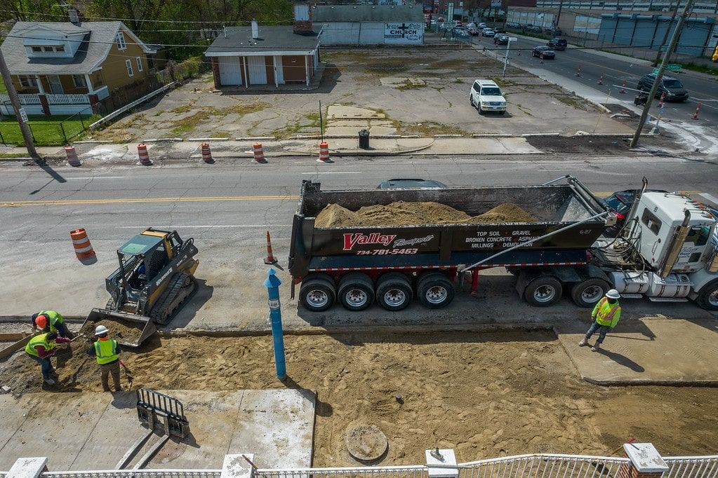 Construction crew working beside a dump truck at a roadwork site, with workers and equipment on a dirt roadway.