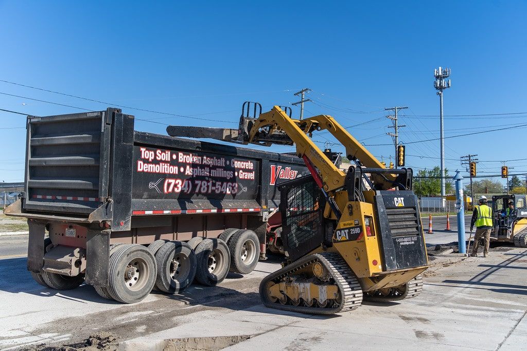 Yellow skid-steer loader beside a black dump truck at a construction site under a clear blue sky