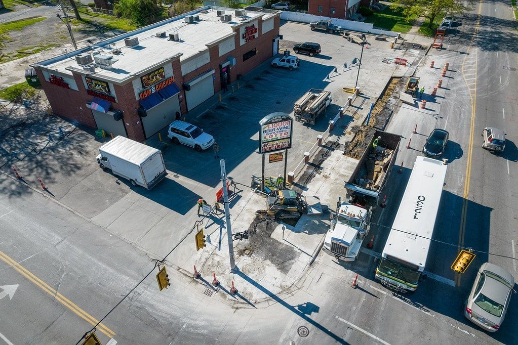 Aerial view of a snowy street corner with a building, parked vehicles, and construction barriers.
