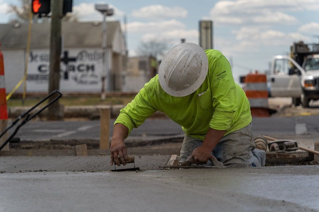 Construction worker in a neon green shirt smoothing wet concrete on a street intersection