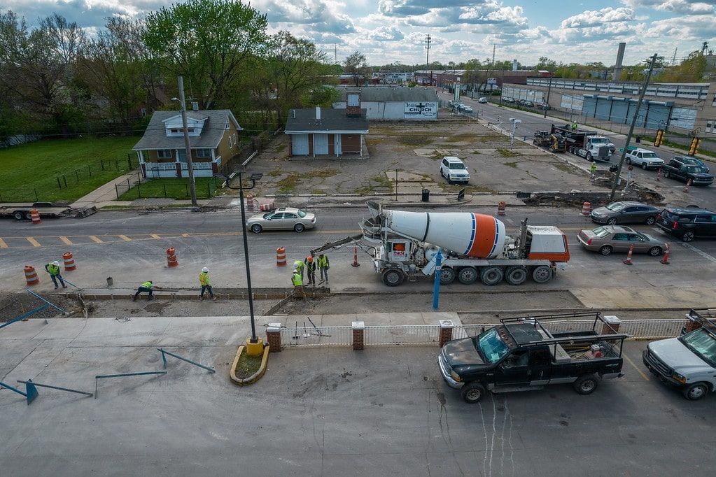 Cement mixer and parked vehicles at a damaged roadside construction site under a cloudy sky