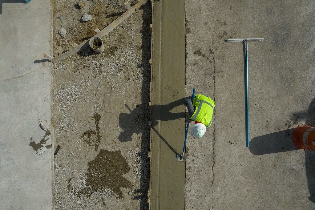 Worker in neon vest painting a concrete surface beside a long crack with tools nearby.