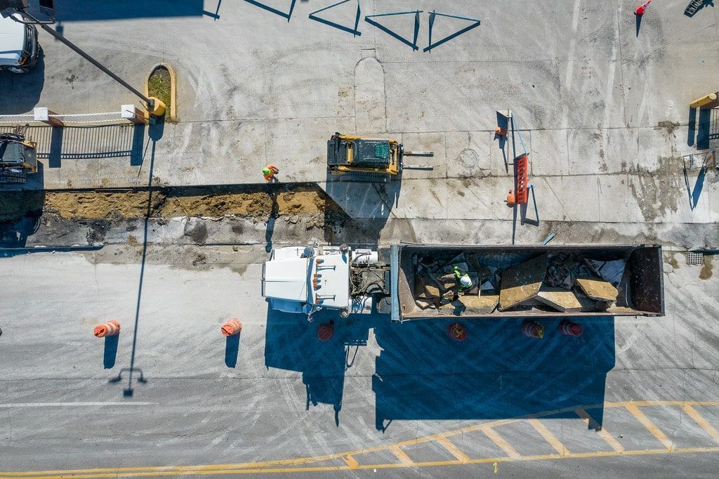 Overhead view of a construction site with workers, equipment, and a large dug trench beside a building