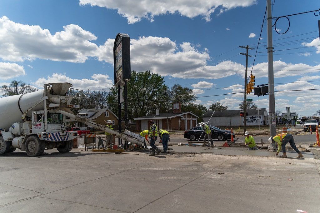 Workers clean up after a cement truck crash on a city street under a blue sky.