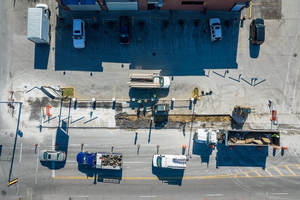 Aerial view of a street with parked vehicles, pedestrians, and a building facade casting shadows