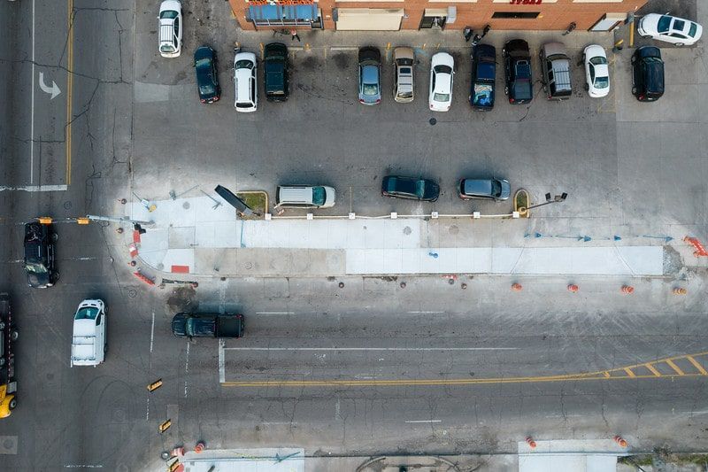 Aerial view of a snowy parking lot and street with parked cars and a long sidewalk barrier