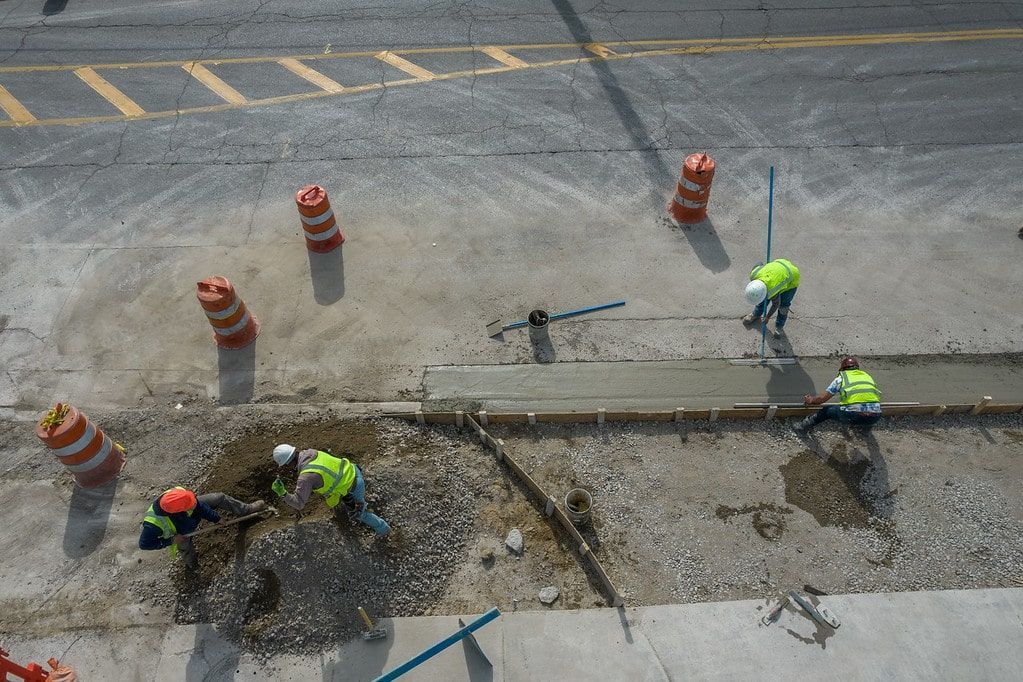 Workers repairing a road trench beside traffic cones on a street.