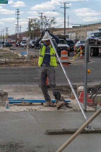 Construction worker in neon vest carrying a metal beam at a roadside work site