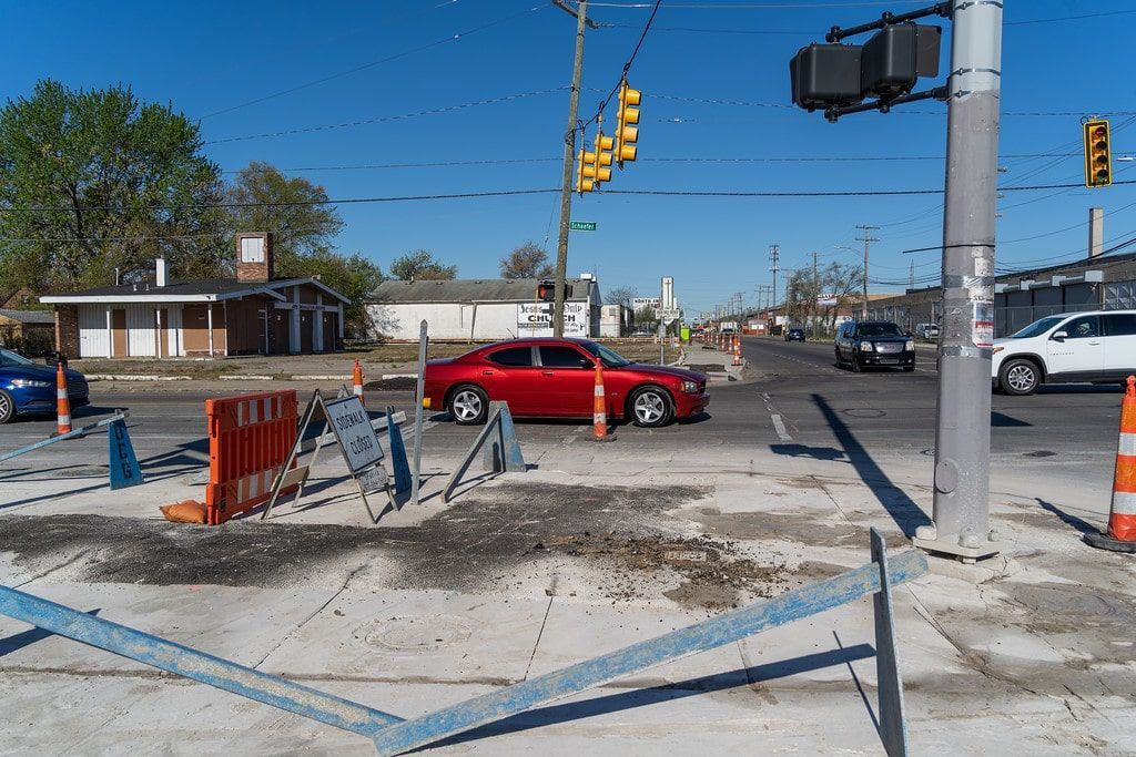 Construction zone at a street intersection with orange barriers, blue tape, and a red car passing under traffic lights