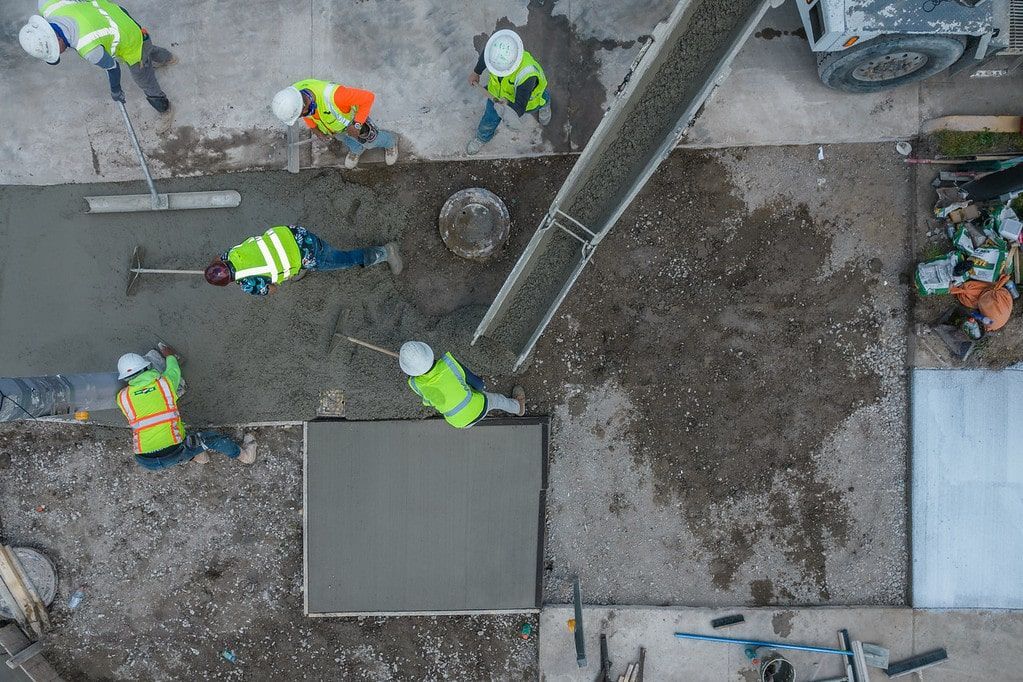 Workers in neon vests working on a muddy construction site near a large pipe.