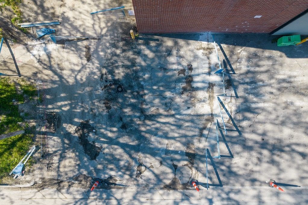 Aerial view of a sandy courtyard with tree shadows, a brick building edge, and scattered playground equipment