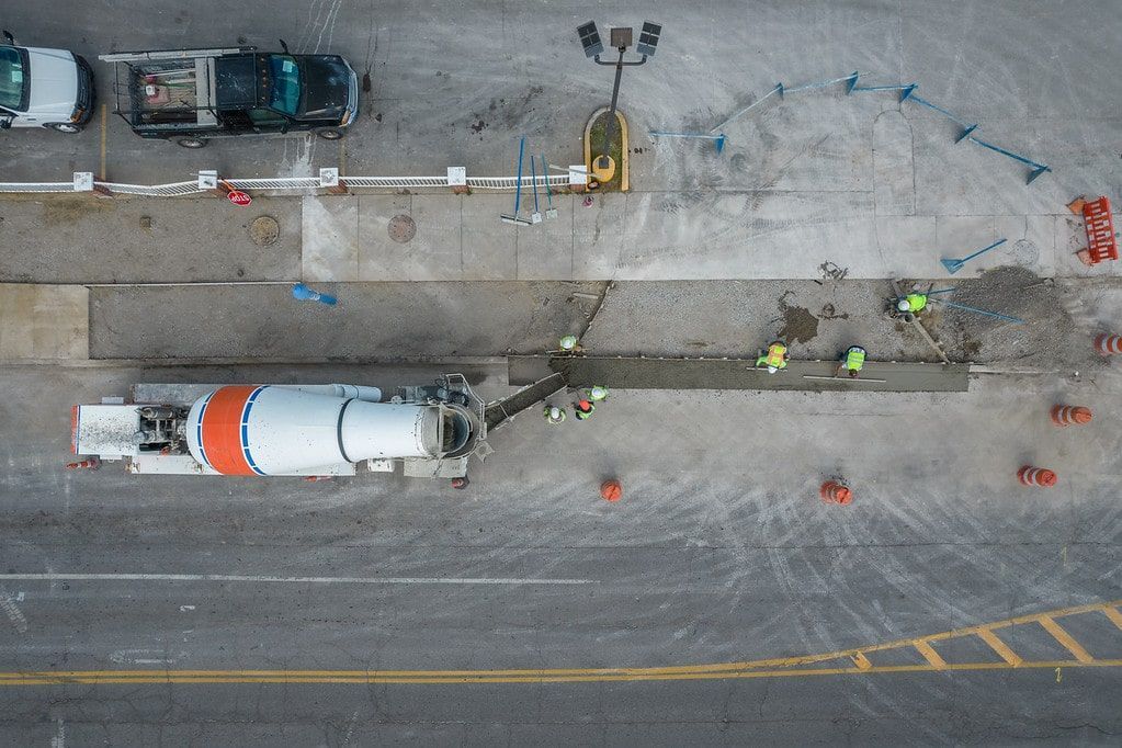 Aerial view of roadwork with a cement mixer truck, workers, cones, and a lane under repair