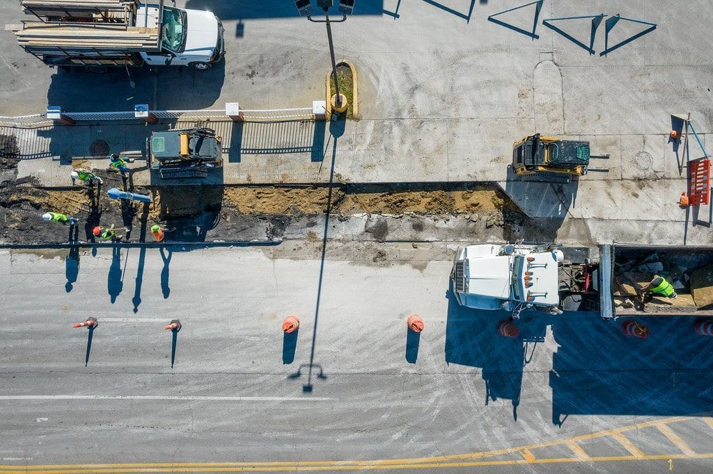 Aerial view of road repair with workers, construction equipment, and fresh asphalt along a street edge