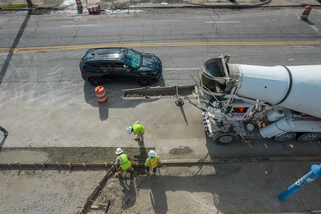 Overhead view of a roadwork scene with workers beside a truck and car on a damaged street.