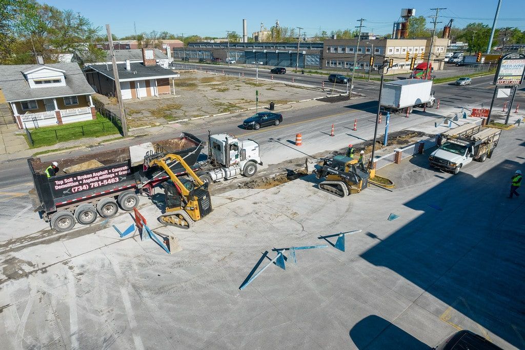 Construction equipment and barriers on a paved lot beside small buildings, with one car and blue sky.