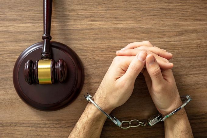 A man in handcuffs is sitting at a wooden table next to a gavel.