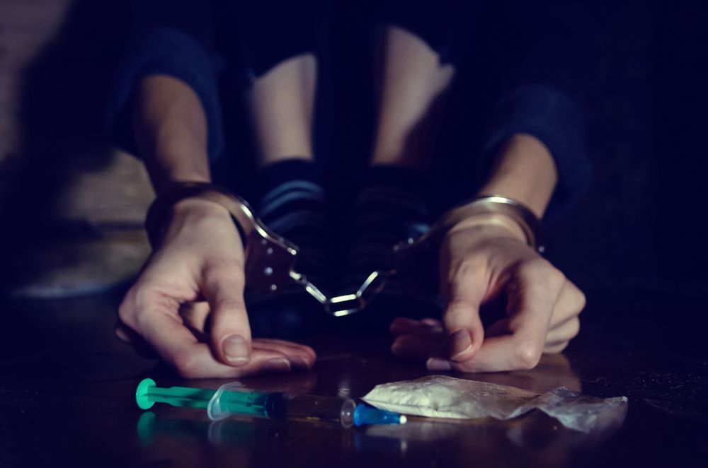 A person in handcuffs is sitting at a table with drugs.