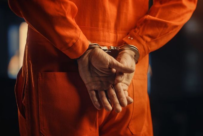 A man in an orange jumpsuit is wearing handcuffs.