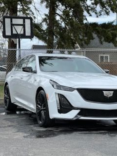 A white car is parked in a parking lot next to a basketball hoop.