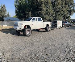 A white truck is parked in a gravel lot next to a trailer.