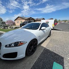 A white car is parked in a driveway next to a trailer.