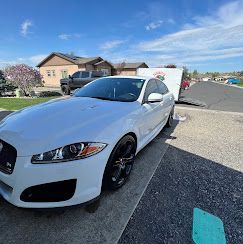 A white car is parked on the side of the road in a parking lot.