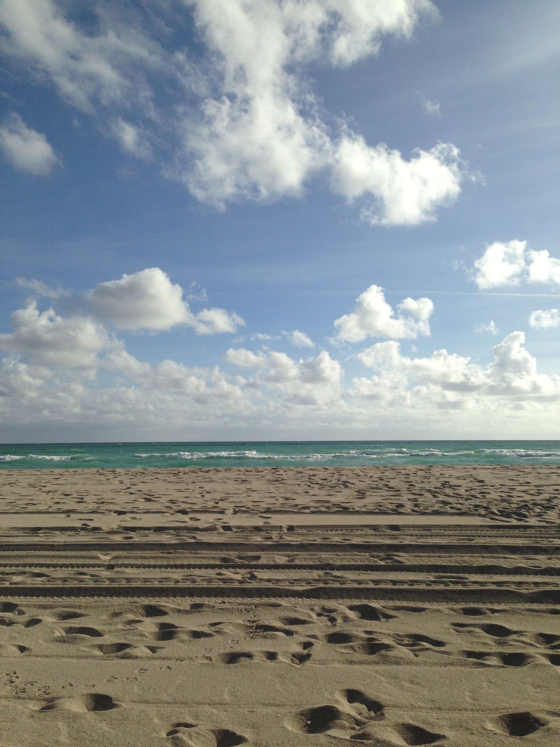 A sandy beach with a blue sky and white clouds