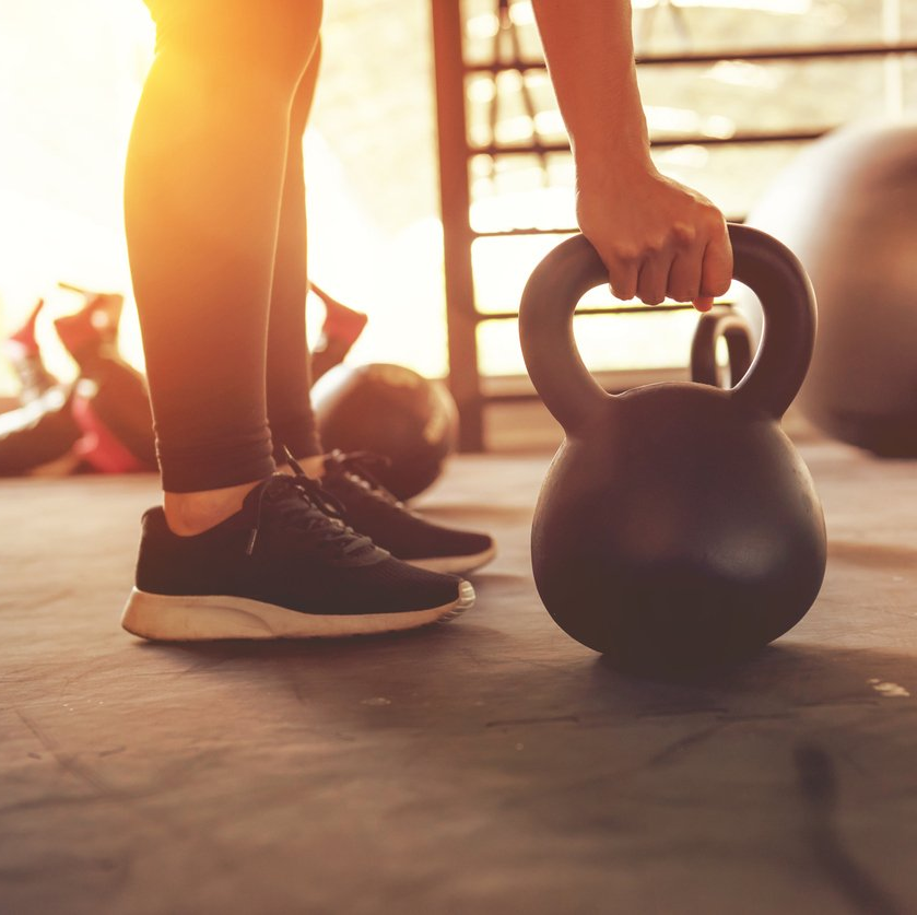 person-feet-in-athletic-shoes-standing-in-gym-at-sunrise-while-grabbing-kettlebell-from-floor