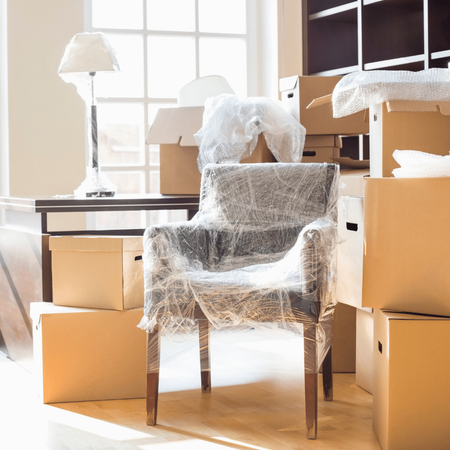 A chair wrapped in plastic is sitting in a room surrounded by cardboard boxes.